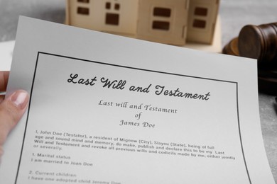 Photo of Woman holding last will and testament at grey table, closeup