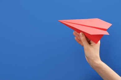 Photo of Woman holding paper plane on blue background, closeup. Space for text