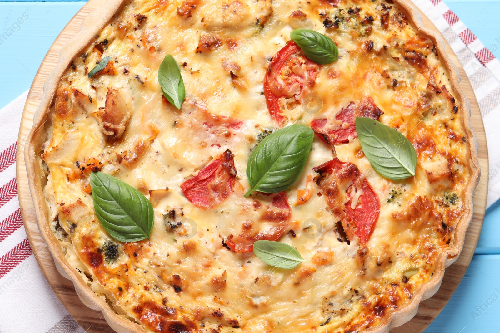 Photo of Tasty quiche with tomatoes, basil and cheese served on light blue wooden table, top view