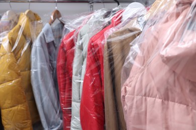Photo of Dry-cleaning service. Hangers with different clothes in plastic bags on rack, closeup