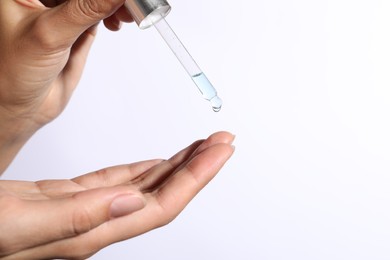 Woman applying cosmetic serum onto her finger on white background, closeup. Space for text