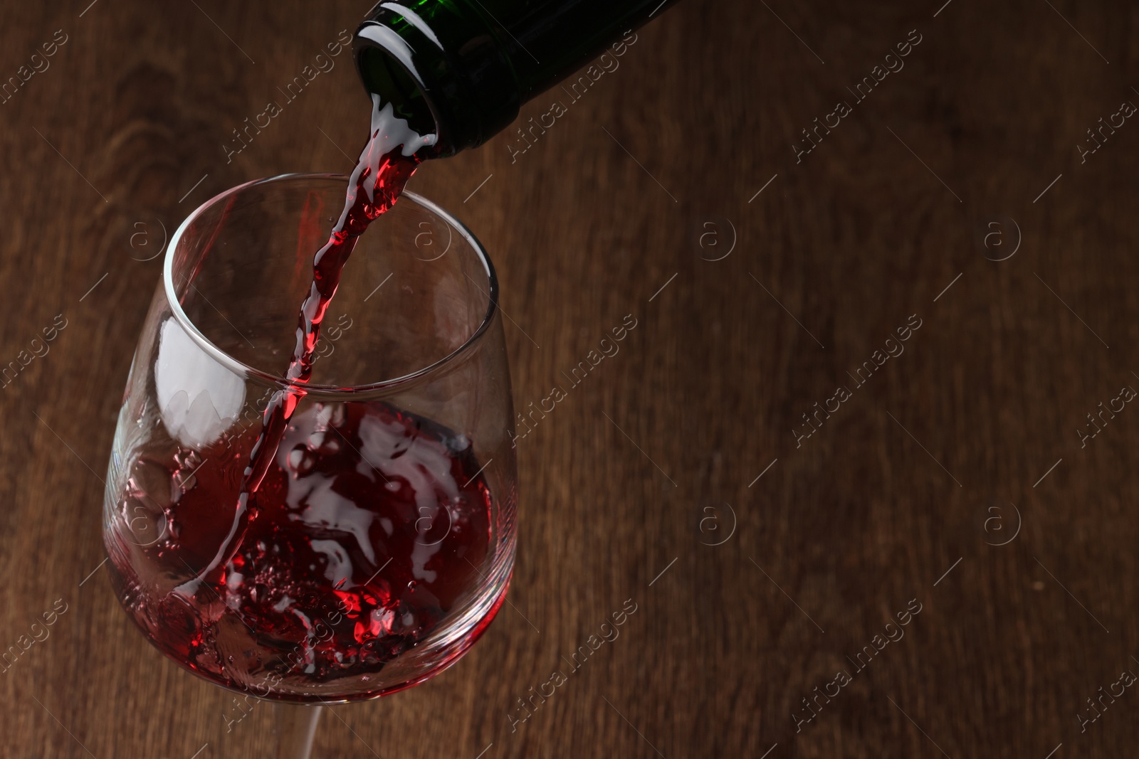 Photo of Pouring tasty red wine in glass at wooden table, closeup. Space for text