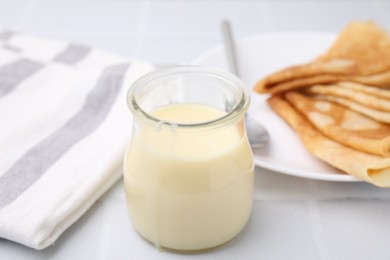 Photo of Tasty condensed milk in jar and crepes on white table, closeup