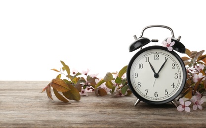 Alarm clock and branch with spring blossoms on wooden table against white background. Time change concept