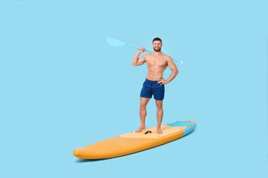 Photo of Happy man with paddle on SUP board against light blue background