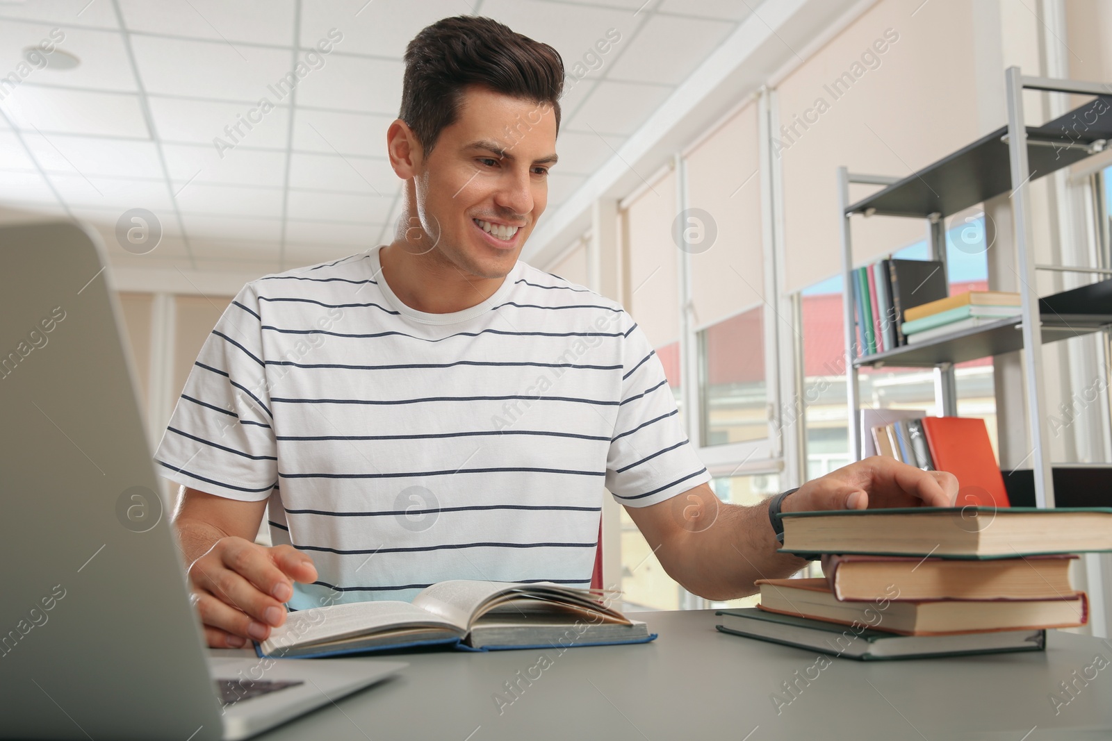 Photo of Man with laptop and books studying at table in library