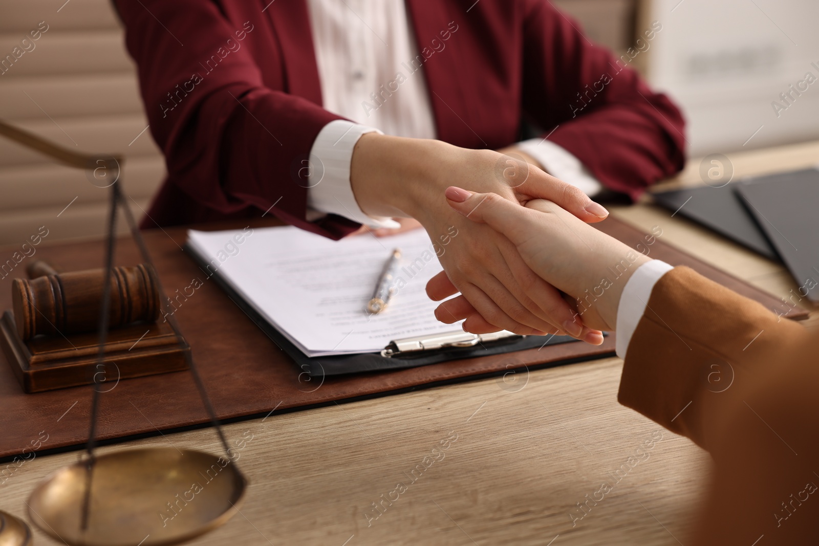 Photo of Notary shaking hands with client at wooden table in office, closeup