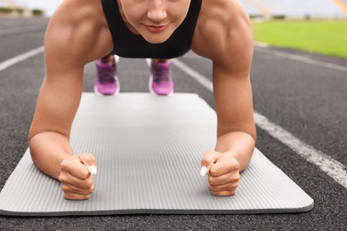 Photo of Young woman doing plank exercise at stadium, closeup
