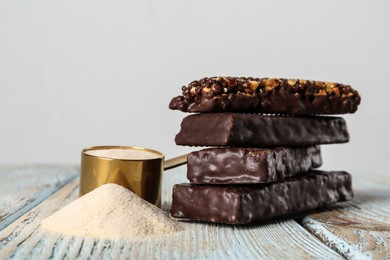 Photo of Different tasty bars and scoop of protein powder on wooden table