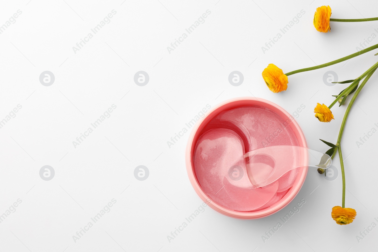 Photo of Jar of under eye patches with spoon and flower on white background, top view with space for text. Cosmetic product