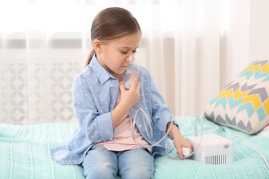 Photo of Sick little girl using nebulizer for inhalation on bed at home