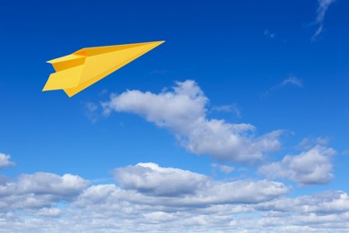 Image of Yellow paper plane flying in blue sky with clouds