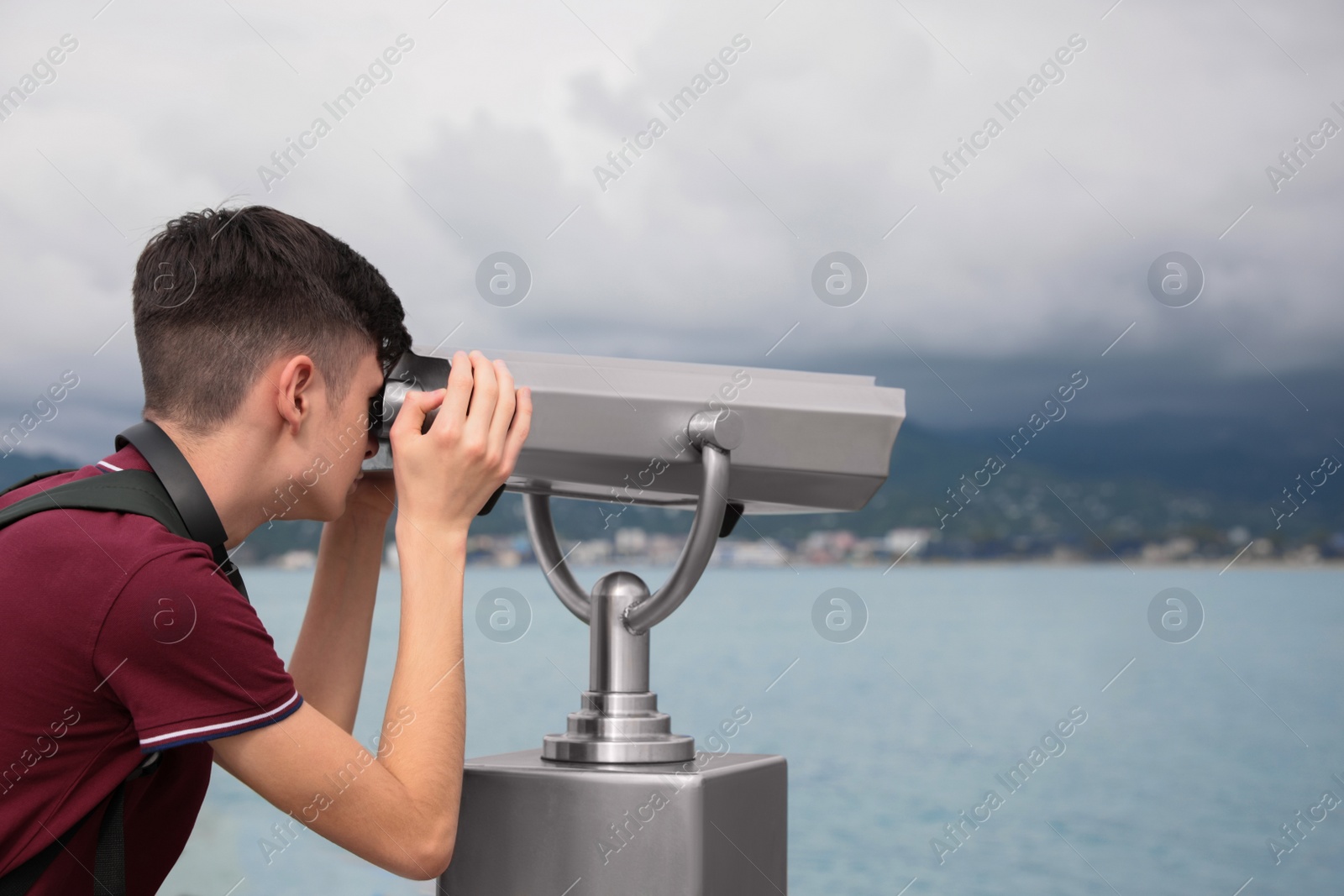 Photo of Teenage boy looking through mounted binoculars at mountains. Space for text