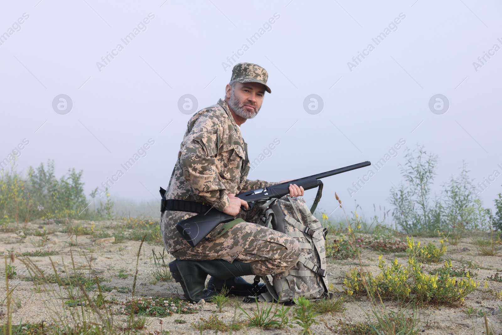 Photo of Man wearing camouflage with hunting rifle and backpack outdoors