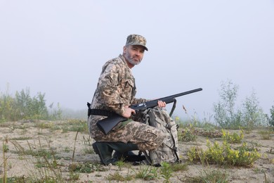 Photo of Man wearing camouflage with hunting rifle and backpack outdoors
