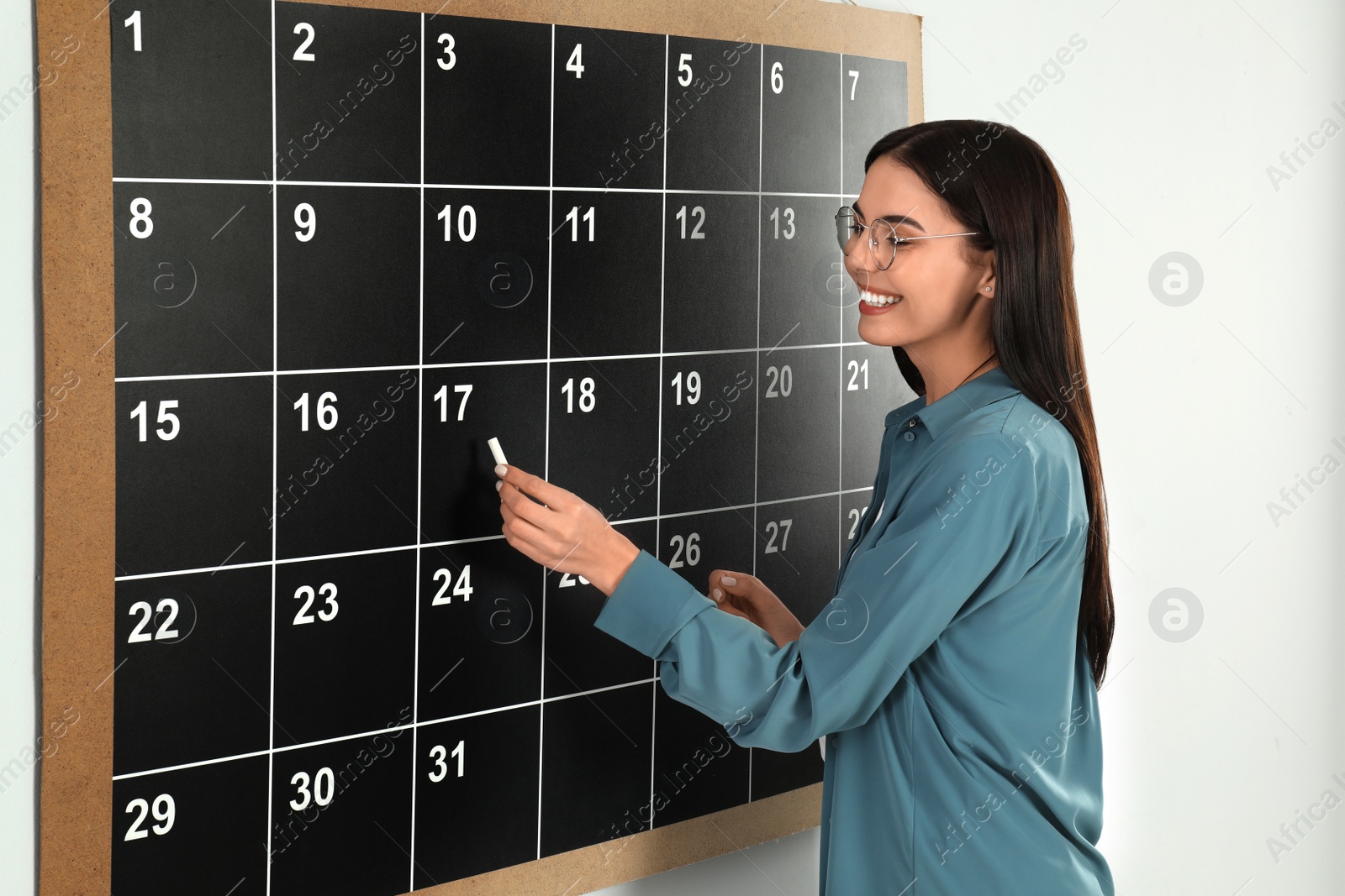 Photo of Young woman writing with chalk on board calendar