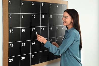 Young woman writing with chalk on board calendar