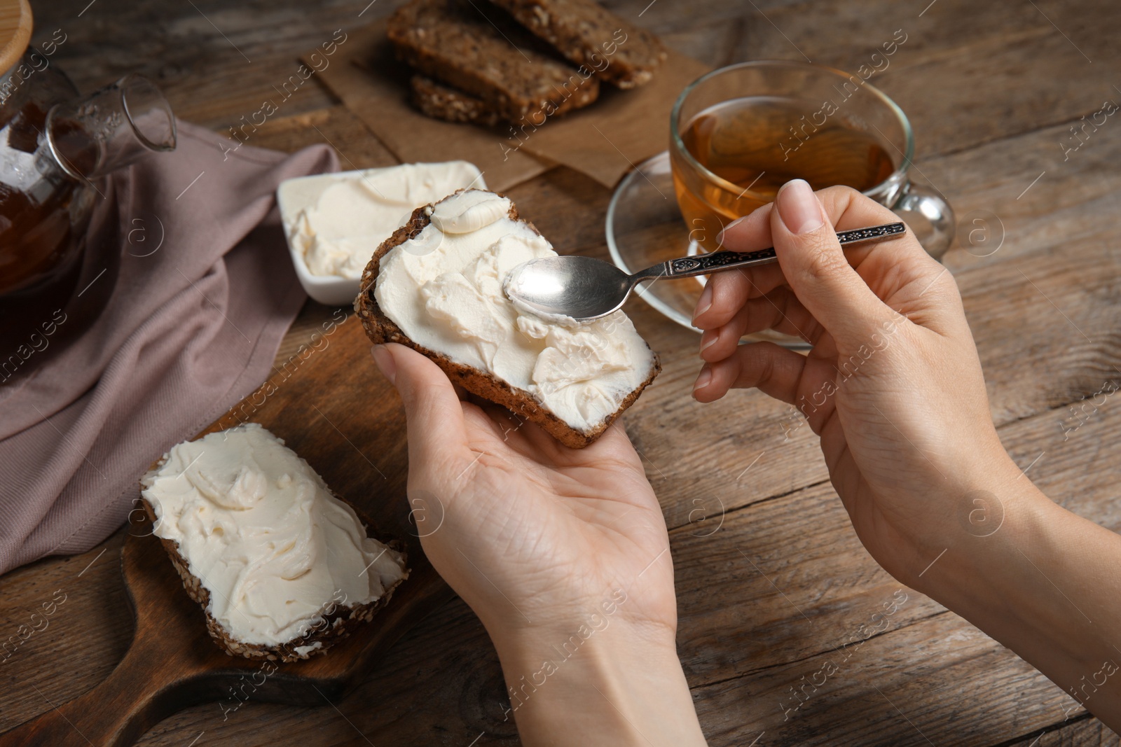 Photo of Woman spreading cream cheese onto bread at wooden table, closeup