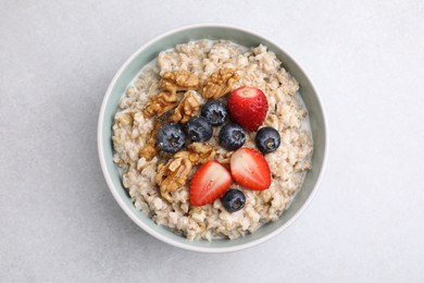 Photo of Tasty oatmeal with strawberries, blueberries and walnuts in bowl on grey table, top view