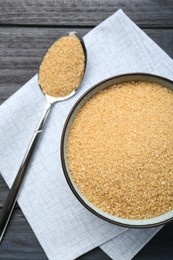 Photo of Brown sugar in bowl and spoon on black wooden table, flat lay