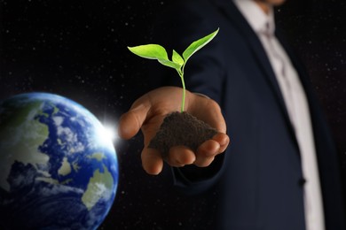 Make Earth green. Man holding soil with seedling, closeup. Black background with globe