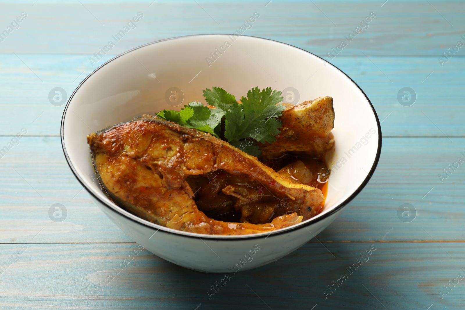 Photo of Tasty fish curry on light blue wooden table, closeup. Indian cuisine