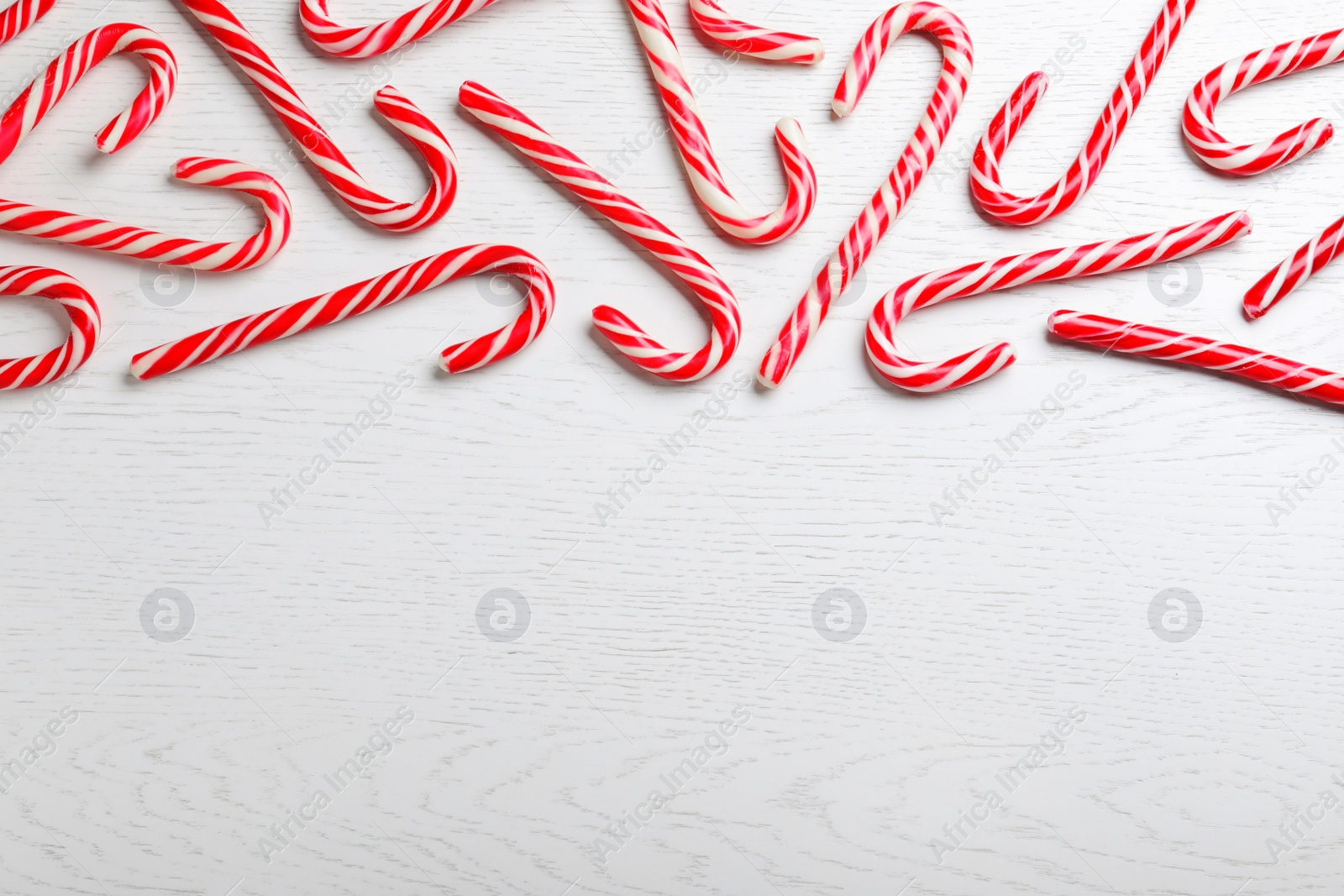 Photo of Sweet Christmas candy canes on white wooden 
background, flat lay. Space for text