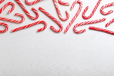 Sweet Christmas candy canes on white wooden 
background, flat lay. Space for text