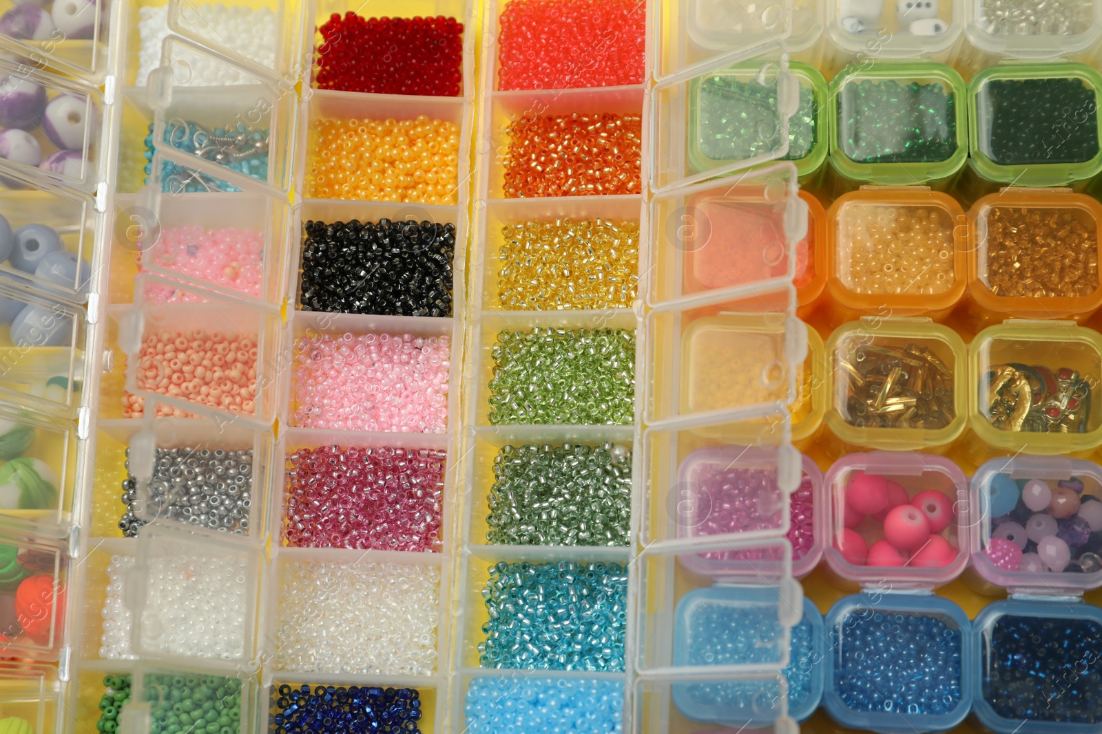 Photo of Organizers with variety of colorful beads on yellow background, above view