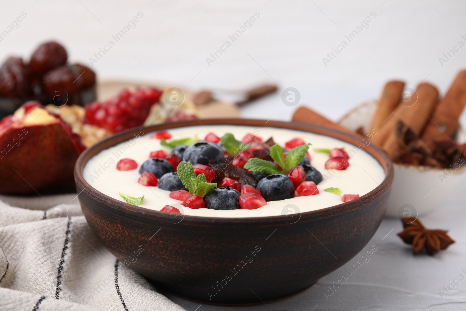 Photo of Delicious semolina pudding with blueberries, pomegranate, dates and mint in bowl on white table, closeup