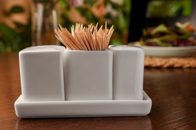 Photo of Holder with salt, pepper and toothpicks on wooden table, closeup