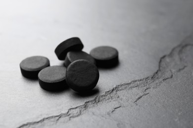 Photo of Activated charcoal pills on black table, space for text. Potent sorbent