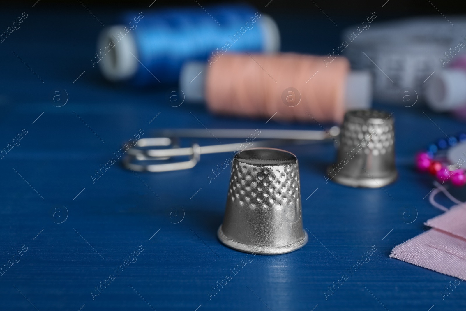 Photo of Silver thimble on blue wooden table, space for text. Sewing accessory