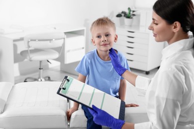 Photo of Endocrinologist with clipboard examining boy's thyroid gland at hospital