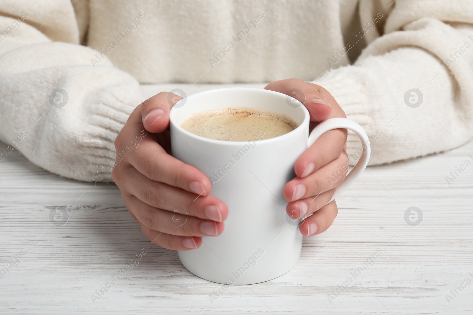 Photo of Woman holding white mug with coffee at wooden table, closeup