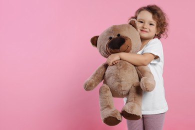 Cute little girl with teddy bear on pink background, space for text