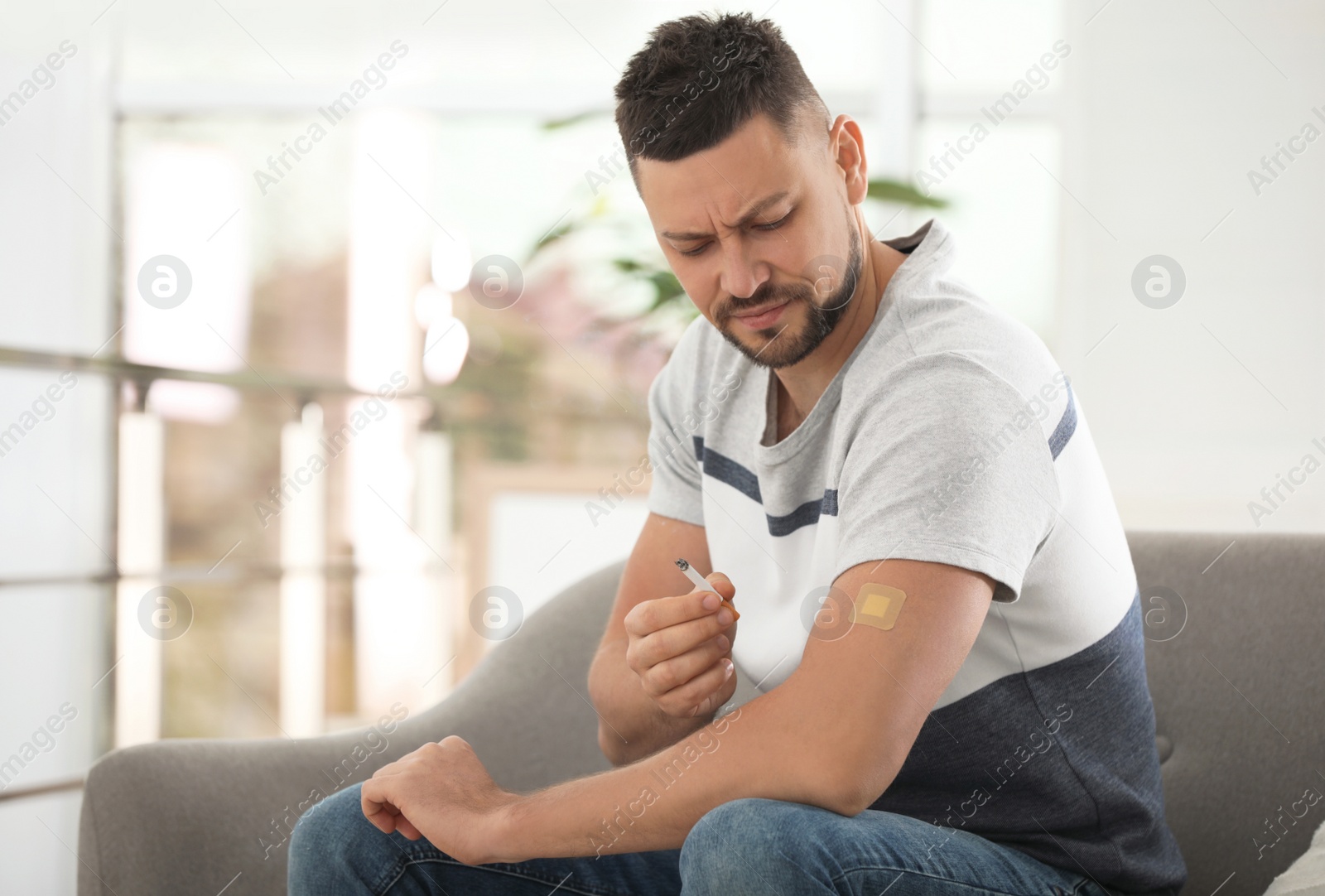 Photo of Emotional man with nicotine patch and cigarette at home