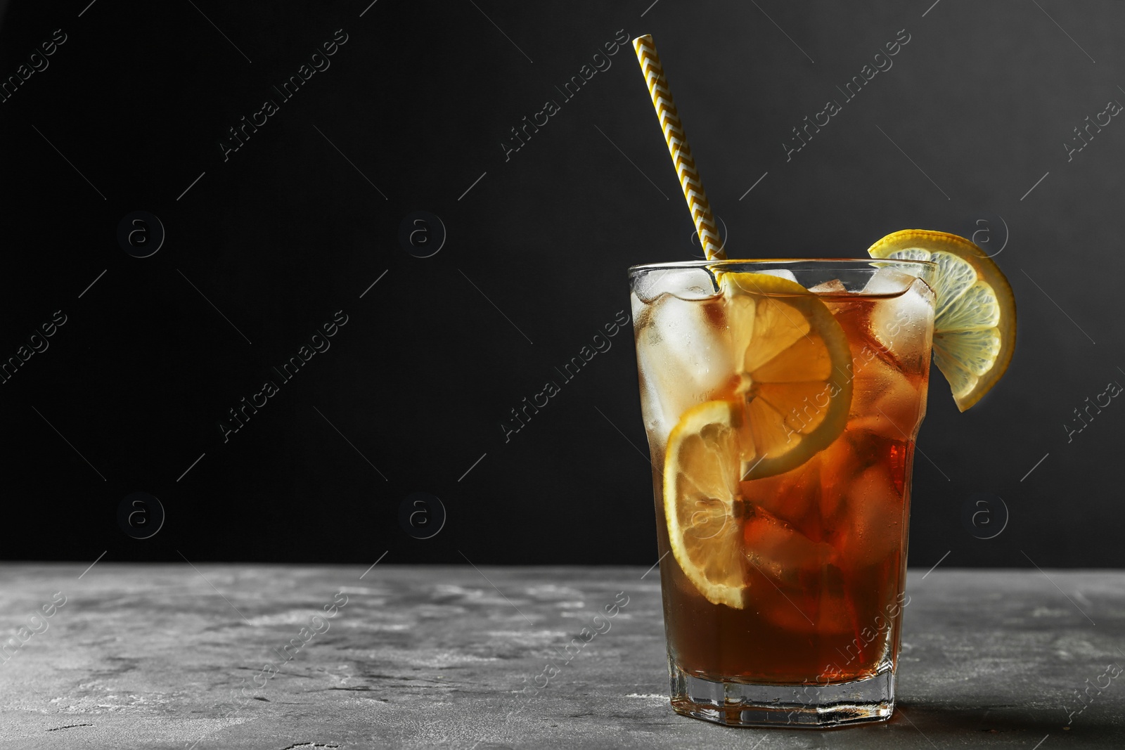 Photo of Glass of delicious iced tea on grey table against black background. Space for text