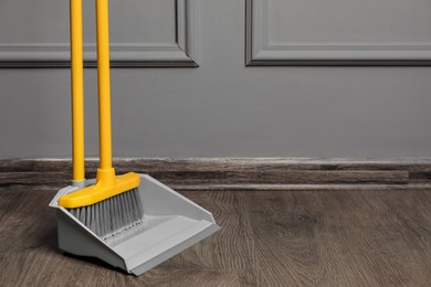 Plastic broom with dustpan near grey wall indoors. space for text