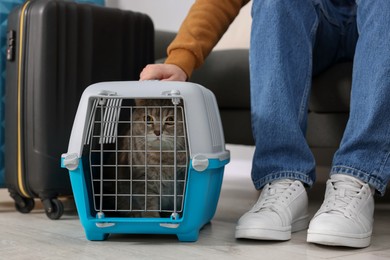 Photo of Travel with pet. Man near carrier with cute cat indoors, closeup