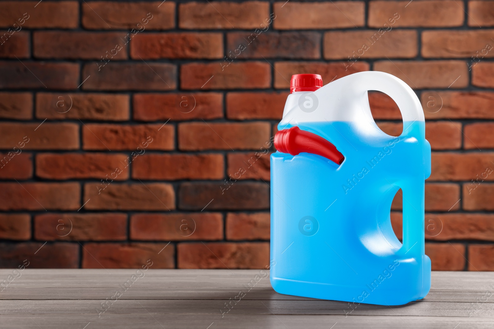 Photo of Plastic canister with blue liquid on wooden table against brick wall, space for text