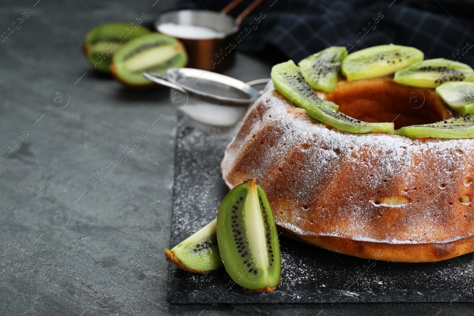 Photo of Homemade yogurt cake with kiwi and powdered sugar on black table, closeup. Space for text