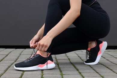 Photo of Woman tying shoelace of sneakers on street, closeup