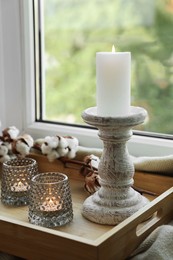 Photo of Beautiful candlestick, scented candles and cotton flowers on wooden tray