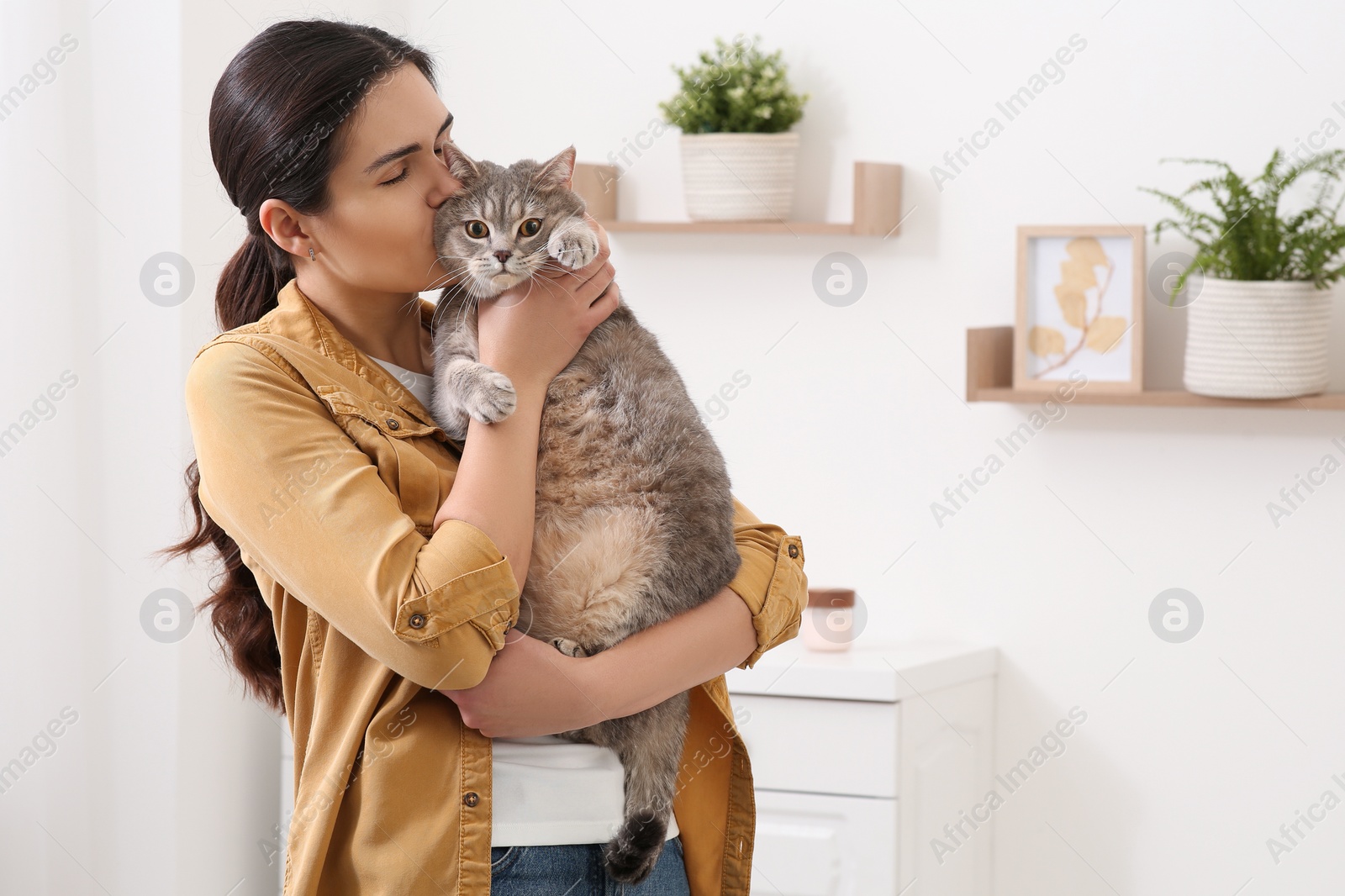 Photo of Young woman kissing her adorable cat at home, space for text