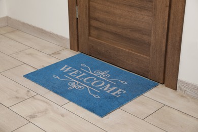 Photo of Beautiful blue doormat with word Welcome on floor near entrance