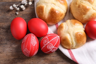 Red painted Easter eggs and buns on wooden table, top view