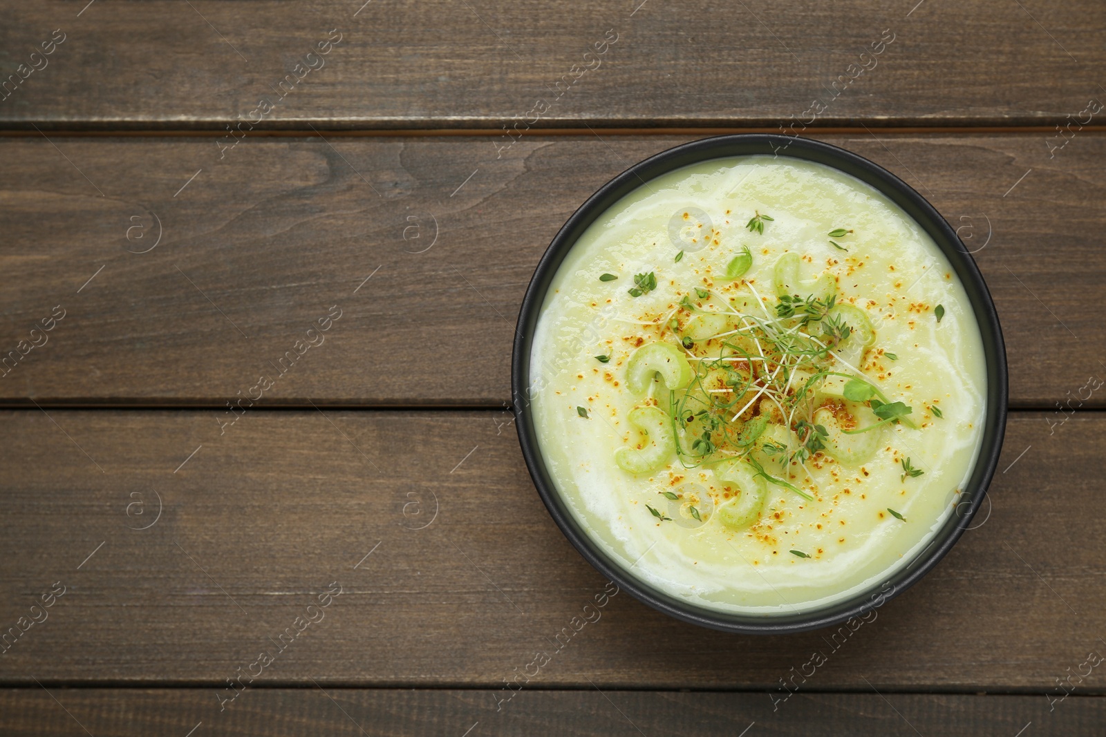 Photo of Bowl of delicious celery soup on wooden table, top view. Space for text