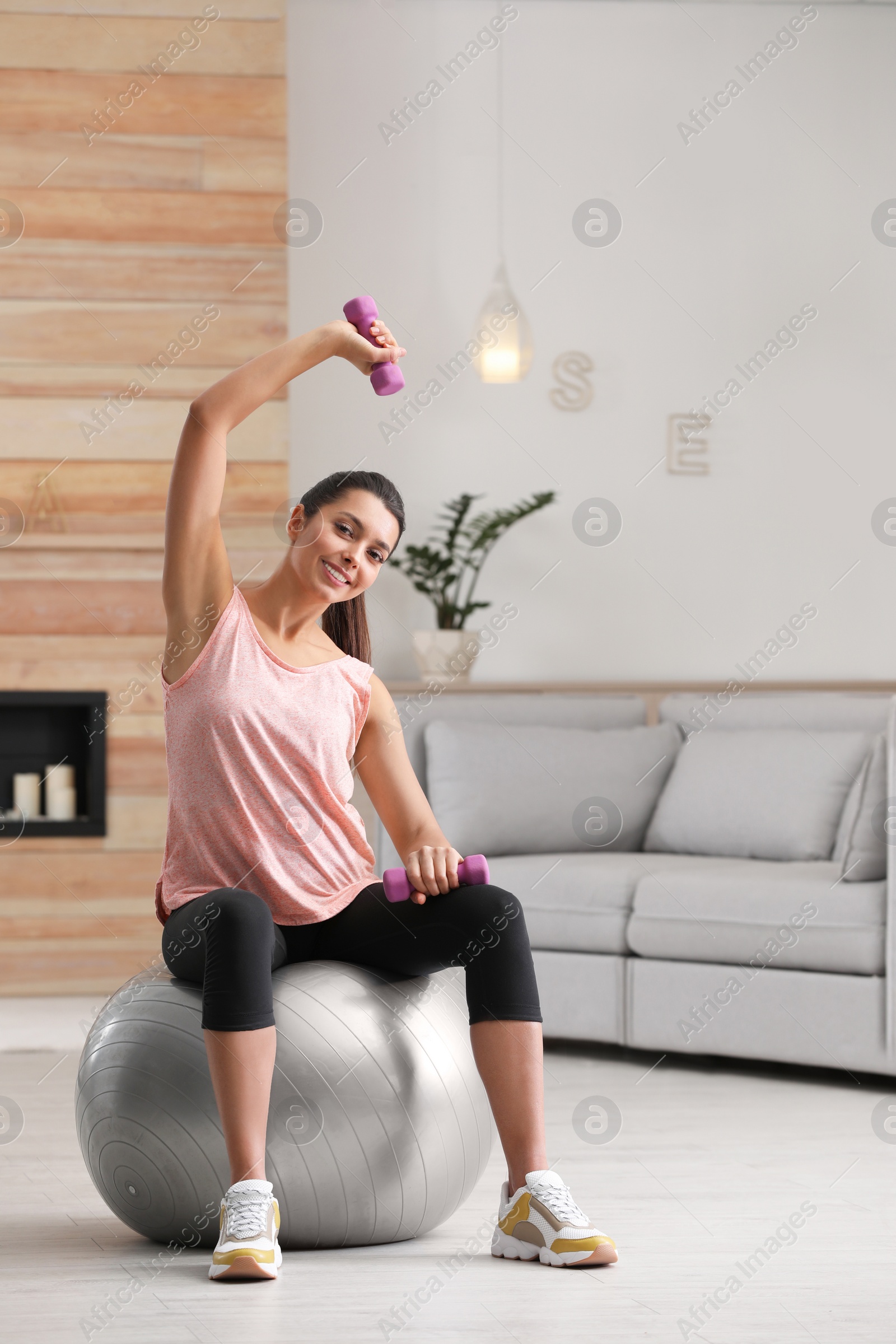 Photo of Young woman doing exercise with dumbbells on fitness ball at home