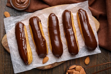 Photo of Delicious eclairs covered with chocolate and almonds on wooden table, flat lay